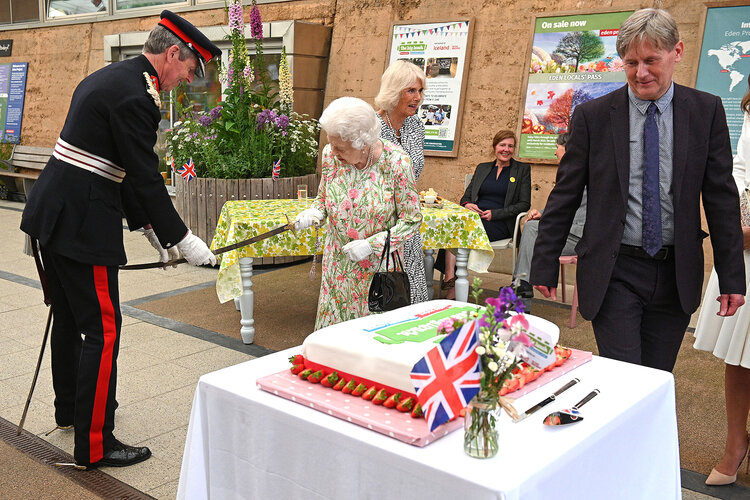 Britain’s Queen Elizabeth II (C) takes a sword from The Lord-Lieutenant of Cornwall, Edward Bolitho (L) in order to cut a cake to celebrate of The Big Lunch initiative at The Eden Project, near St Austell in south west England on June 11, 2021.